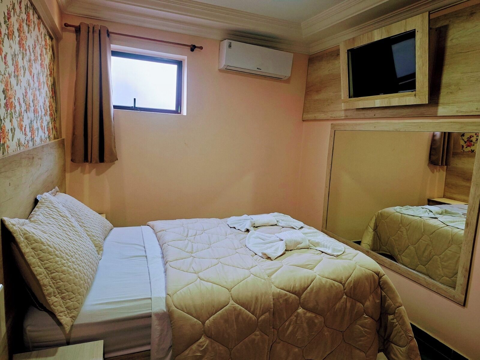 A bedroom with a bed, a window, an air conditioner, and a television.