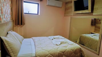 A bedroom with a bed, a window, an air conditioner, and a television.