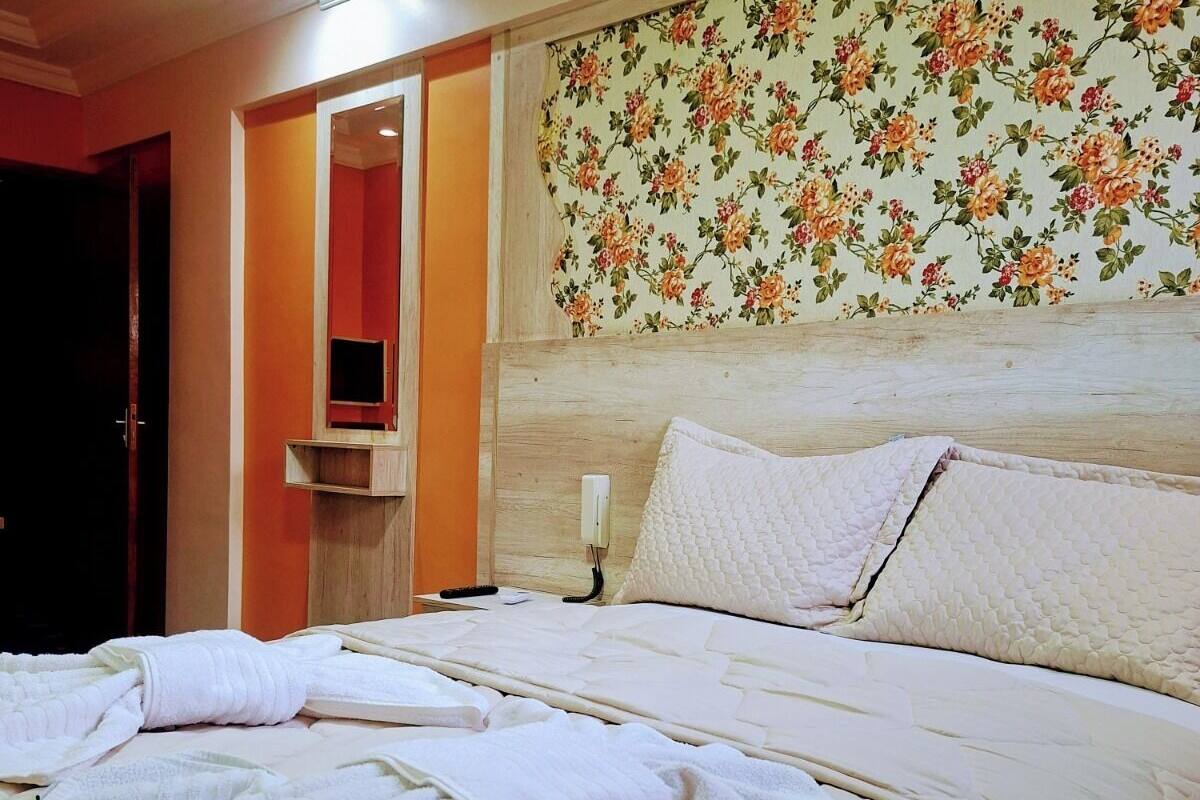 Una habitación de hotel con cama, espejo, mesita de noche y papel tapiz floral.
