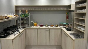 Une cuisine compacte équipée d’une cuisinière à gaz, d’une machine à café et de divers produits alimentaires disposés sur le plan de travail.