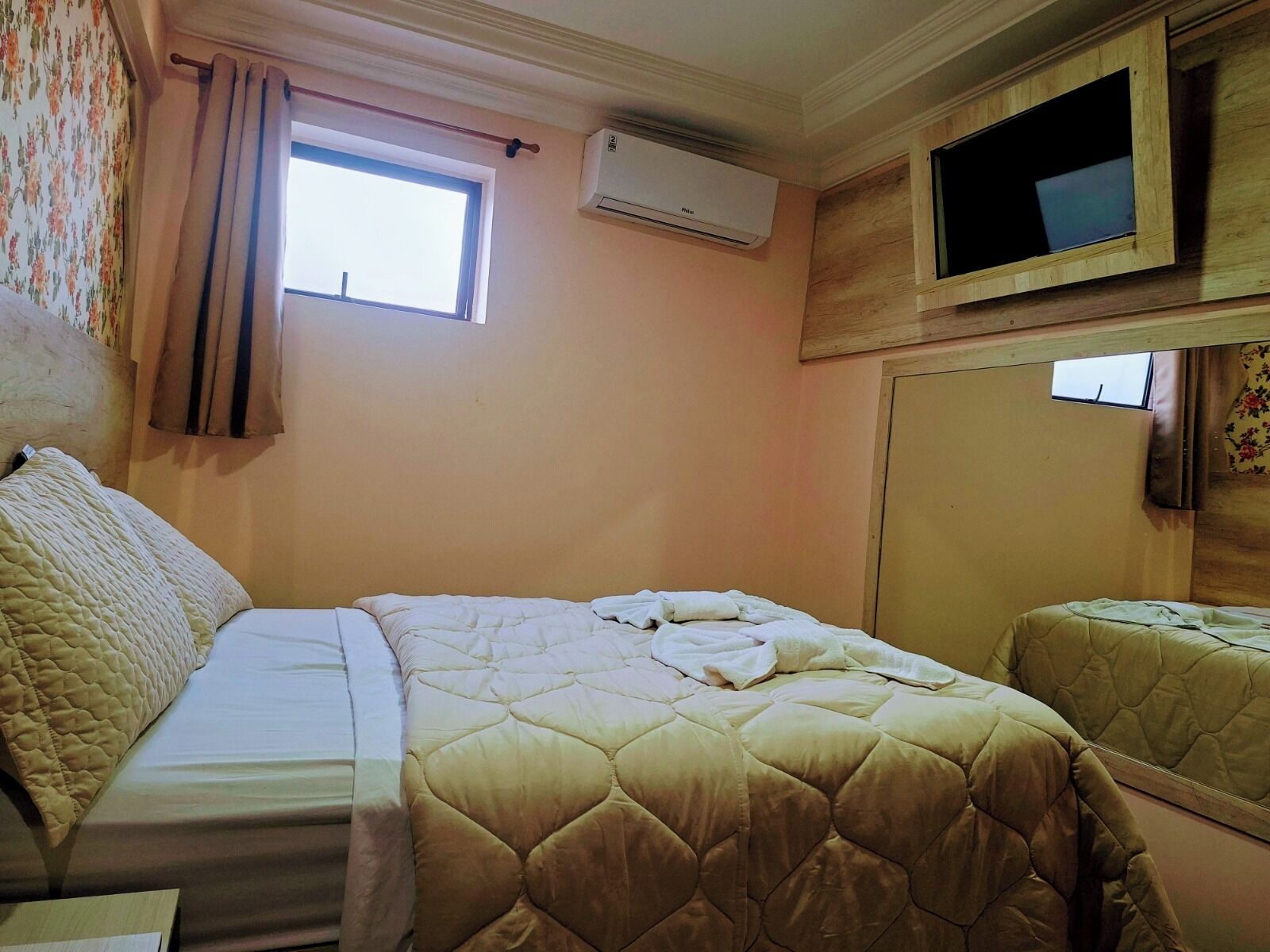 A bedroom with a bed, a window, an air conditioner, and a television.