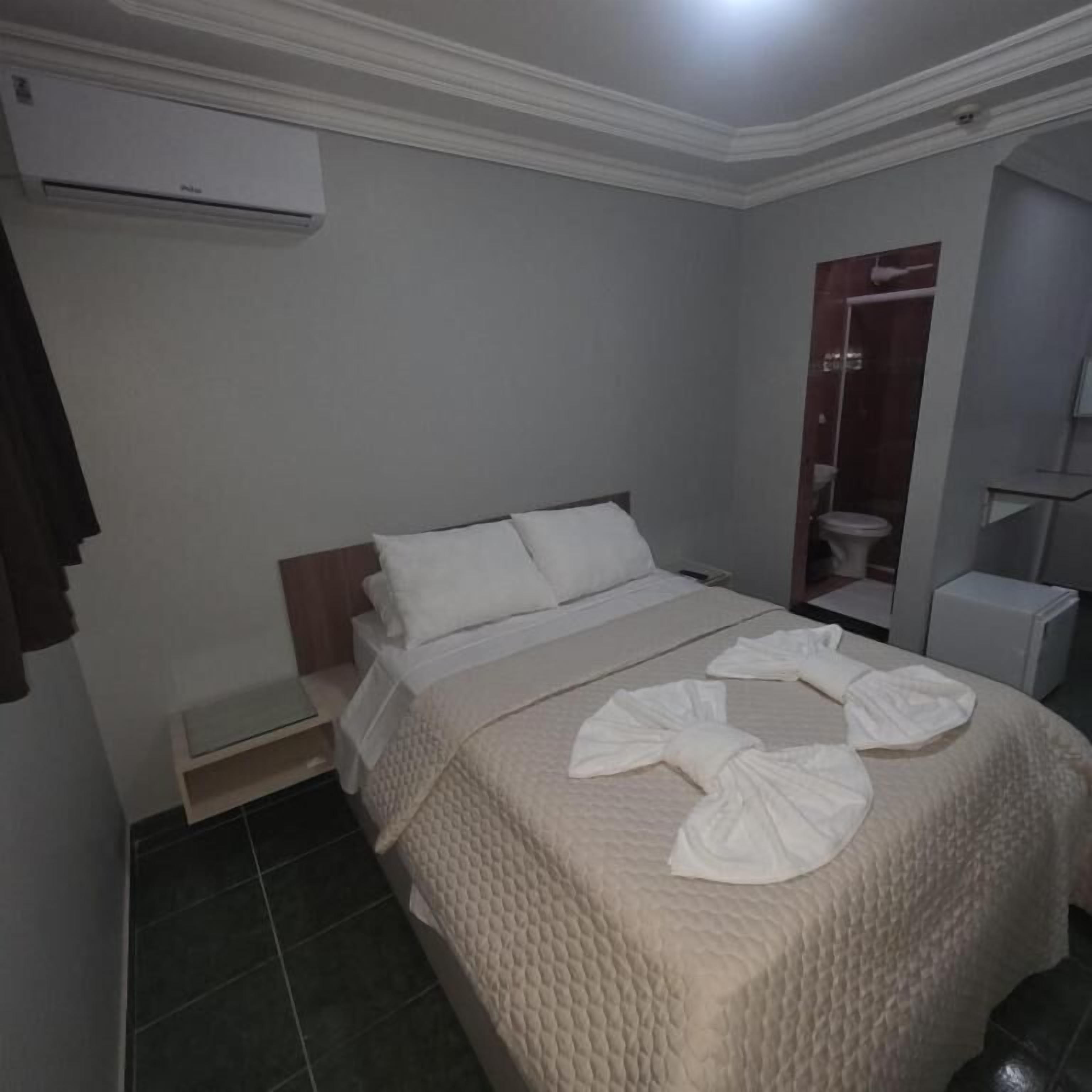 A hotel room with a bed, a bedside table, an air conditioning unit, a shower area, and a wardrobe.