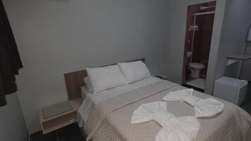 A hotel room with a bed, a bedside table, an air conditioning unit, a shower area, and a wardrobe.