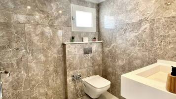 A modern bathroom with a marble wall, a built-in toilet, a shower area, and a vanity with a sink.