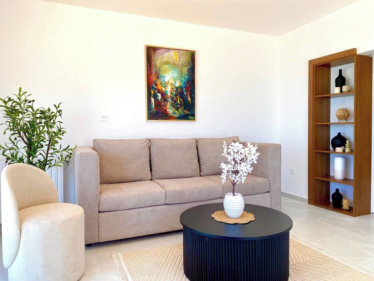 A living room with a sofa, a round coffee table, a chair, a bookshelf, and a painting on the wall.