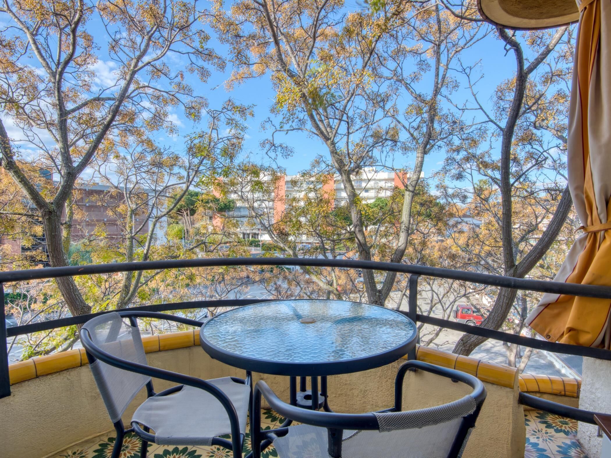 A balcony with a round table and chairs, overlooking a cityscape with trees and buildings.