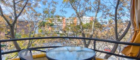 A balcony with a round table and chairs, overlooking a cityscape with trees and buildings.