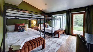 A room with bunk beds, a desk, a chair, and a view of the outdoors.