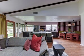 Una sala de estar moderna con un sofá, un comedor con sillas, una cocina con barra y ventanas amplias.