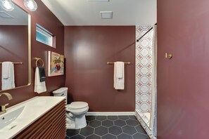 Une salle de bain avec un lavabo blanc, des toilettes, une douche aux carreaux décorés et un miroir avec éclairage.