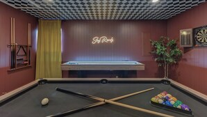 A pool table with a neon sign, a dartboard, and a billiards rack.