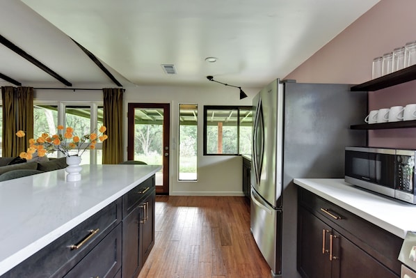 Una cocina moderna con armarios oscuros, un refrigerador de acero inoxidable, un microondas y un amplio ventanal con cortinas.