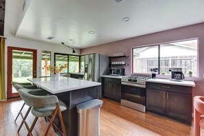 Una cocina moderna con una isla central, armarios oscuros, electrodomésticos de acero inoxidable y un amplio ventanal.
