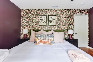 Una cama bien hecha con almohadas decorativas, una lámpara de noche y un cuadro en la pared.
