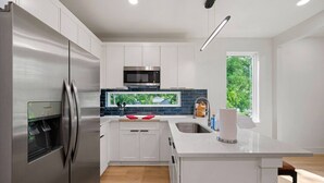 Una cucina moderna con mobili bianchi, elettrodomestici in acciaio inossidabile, un dispenser di acqua integrato e un'ampia finestra con vista sul verde.