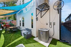 A backyard with a patio, outdoor seating, a large air conditioning unit, and a fan. - Suite Duplex @Downtown Unit B 6 Br/6 Bath (Houston)
