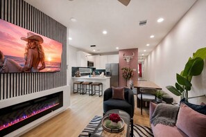 Un salon moderne avec une cheminée, un téléviseur fixé au mur et un coin repas avec une cuisine en arrière-plan.
