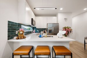 Une cuisine moderne dotée d’un îlot central, d’appareils électroménagers en acier inoxydable et d’un animal en peluche décoratif.