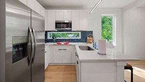 Una cucina moderna con elettrodomestici in acciaio inossidabile, mobili bianchi, un forno a microonde integrato e una finestra vista sul verde.