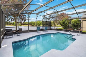 A covered swimming pool with chairs and a table, surrounded by trees and a clear sky.