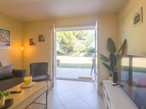 Ein Wohnzimmer mit einer Couch, einem Couchtisch, einem Fernseher und einer Tür, die auf eine Terrasse führt.