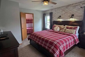 Ein Schlafzimmer mit Bett, Schreibtisch, Kleiderschrank, einer Tür zu einem anderen Raum und einem Deckenventilator.