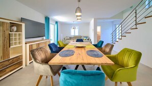 Uma sala de estar moderna com uma mesa de jantar de madeira, cadeiras coloridas, um sofá e uma TV.