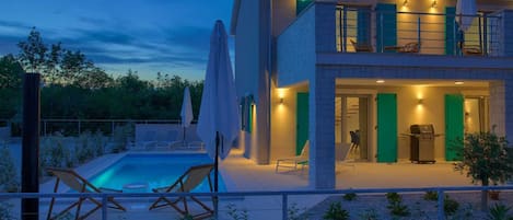 A modern two-story house with a swimming pool, outdoor seating, and a barbecue area.