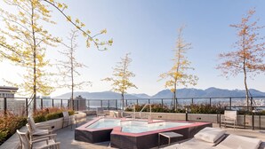 A rooftop terrace with a hot tub, lounge chairs, and a view of mountains. - Charming Apartment Gastown Downtown FIFA (Vancouver)