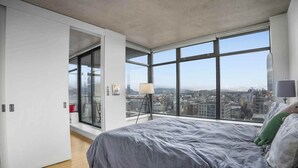 A modern bedroom with a large bed, a view of the city through floor-to-ceiling windows, and a sliding door leading to a balcony. - Charming Apartment Gastown Downtown FIFA (Vancouver)