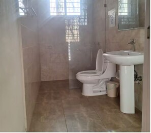 A bathroom with a toilet, sink, and a small trash bin. - Studio with a bed, bathroom, kitchen and a private balcony. (Santo Domingo)