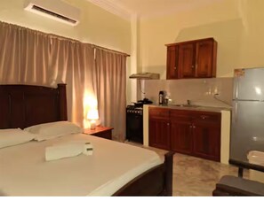 A hotel room with a bed, a desk, a kitchenette, and a refrigerator. - Studio with a bed, bathroom, kitchen and a private balcony. (Santo Domingo)