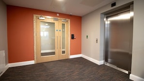 A hallway with an elevator, a wooden door with frosted glass panels, and a carpeted floor. - The Maltings  (Portlaoise)