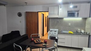 A compact kitchen with a gas stove, microwave, and a small sink. There is a dining area with a table and chairs. - Centrally located apartment, which allows your pet. (Mendoza)