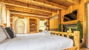 A wooden cabin-style bedroom with a bed, a hanging chair, a fireplace, and a TV mounted on the wall. - The Magic Cottage: Artsy Nashville Escape w/ Hot Tub, Sleeps 10, & Near Downtown (Nashville)