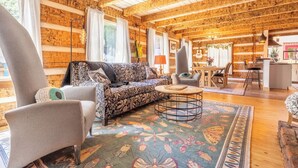 A cozy cabin interior with a wooden ceiling, a patterned sofa, a round coffee table, and a dining area. - The Magic Cottage: Artsy Nashville Escape w/ Hot Tub, Sleeps 10, & Near Downtown (Nashville)