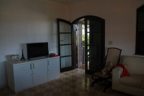 Ein Zimmer mit Fernseher auf einem Schrank, einem Sessel und einer Tür zu einem Außenbereich.