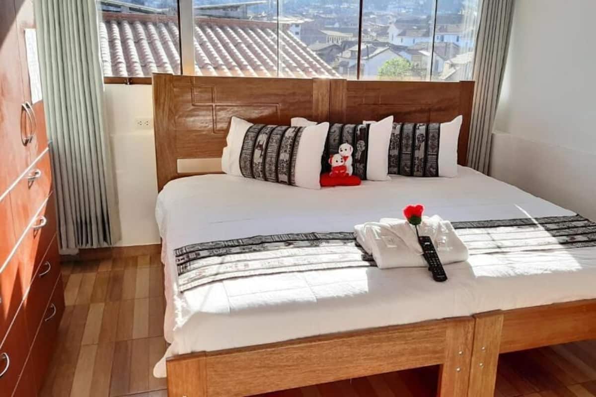 A neatly made bed with a wooden headboard, a white comforter, and a red teddy bear.