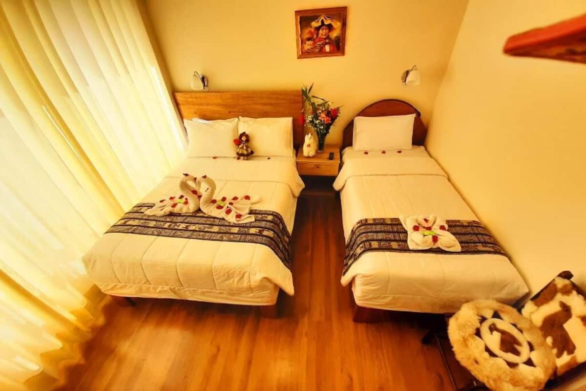 A hotel room with two beds, a wooden floor, a nightstand with a vase, and a painting on the wall.