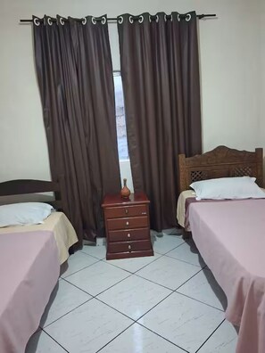 A room with two beds, a wooden dresser, and a window with curtains.