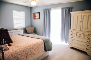 A bedroom with a bed, a dresser, a window with blinds, a lamp, and a framed picture on the wall.