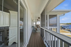 A covered porch with a view of a lake, wooden deck, and outdoor furniture.
