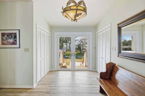 A hallway with a wooden bench, a chandelier, and a view through glass doors to an outdoor area.