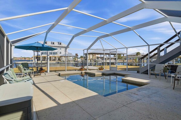 Une piscine extérieure entourée d’une structure métallique blanche, avec des chaises longues et des parasols.