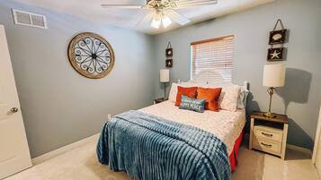 A bedroom with a bed, a ceiling fan, a wall clock, and a window with blinds.