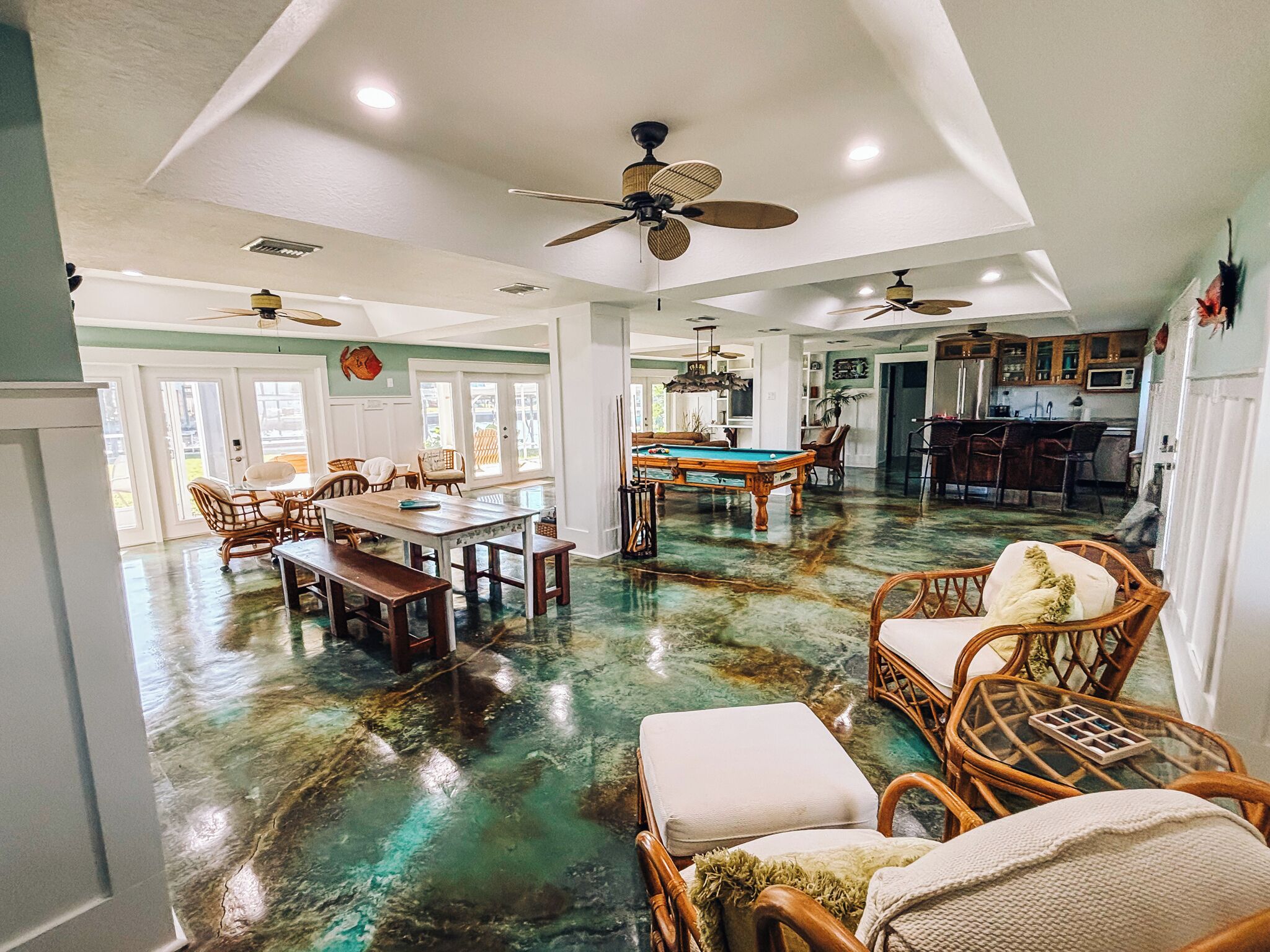 A spacious living area with a pool table, comfortable seating, and a kitchen in the background.