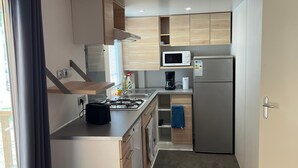 Eine kleine Küche mit Gasherd, Mikrowelle, Kühlschrank und Holzschränken.