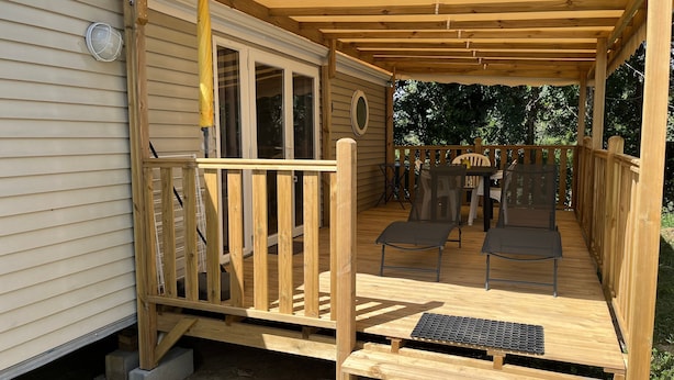 Eine Holzterrasse mit Geländer, zwei Stühlen und einem Tisch.