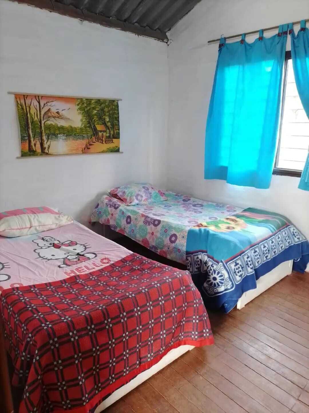 Quarto com duas camas, um quadro na parede e uma janela com cortinas azuis.