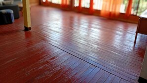A room with a wooden floor, a chair, and a window with red curtains.